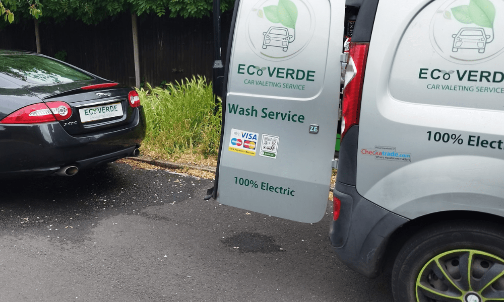 About Us 25 A black car and a light grey EcoVerde car valeting van are parked on a leafy Hampton street. The van’s open door displays the company’s green logo, wash service details, and a 100% electric sign.